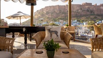 An outdoor seating area with wicker furniture, a piano, and a view of a mountainous landscape.