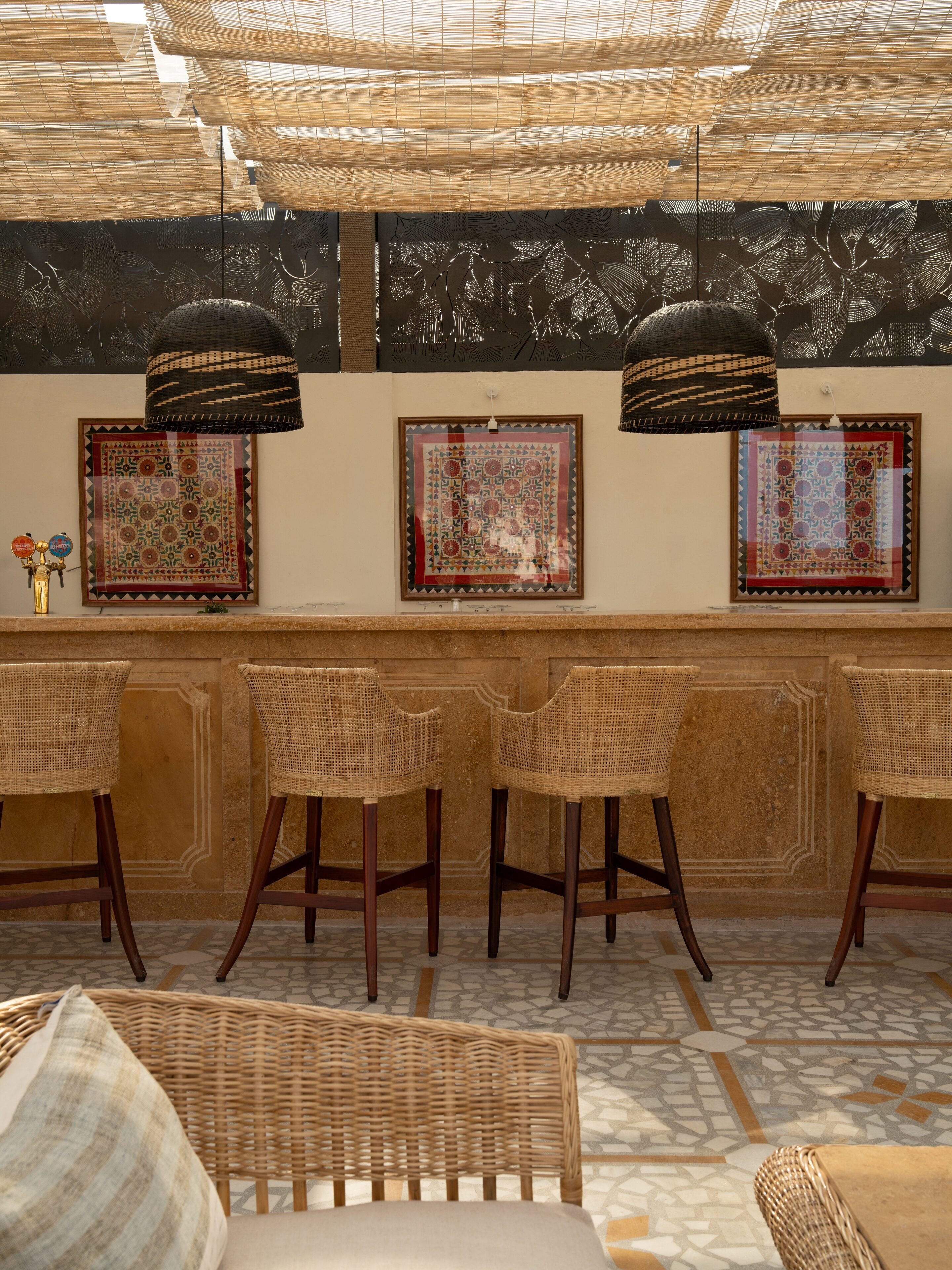 Eine Bar mit Korbstühlen, gefliestem Boden und gerahmten Wandbildern.
