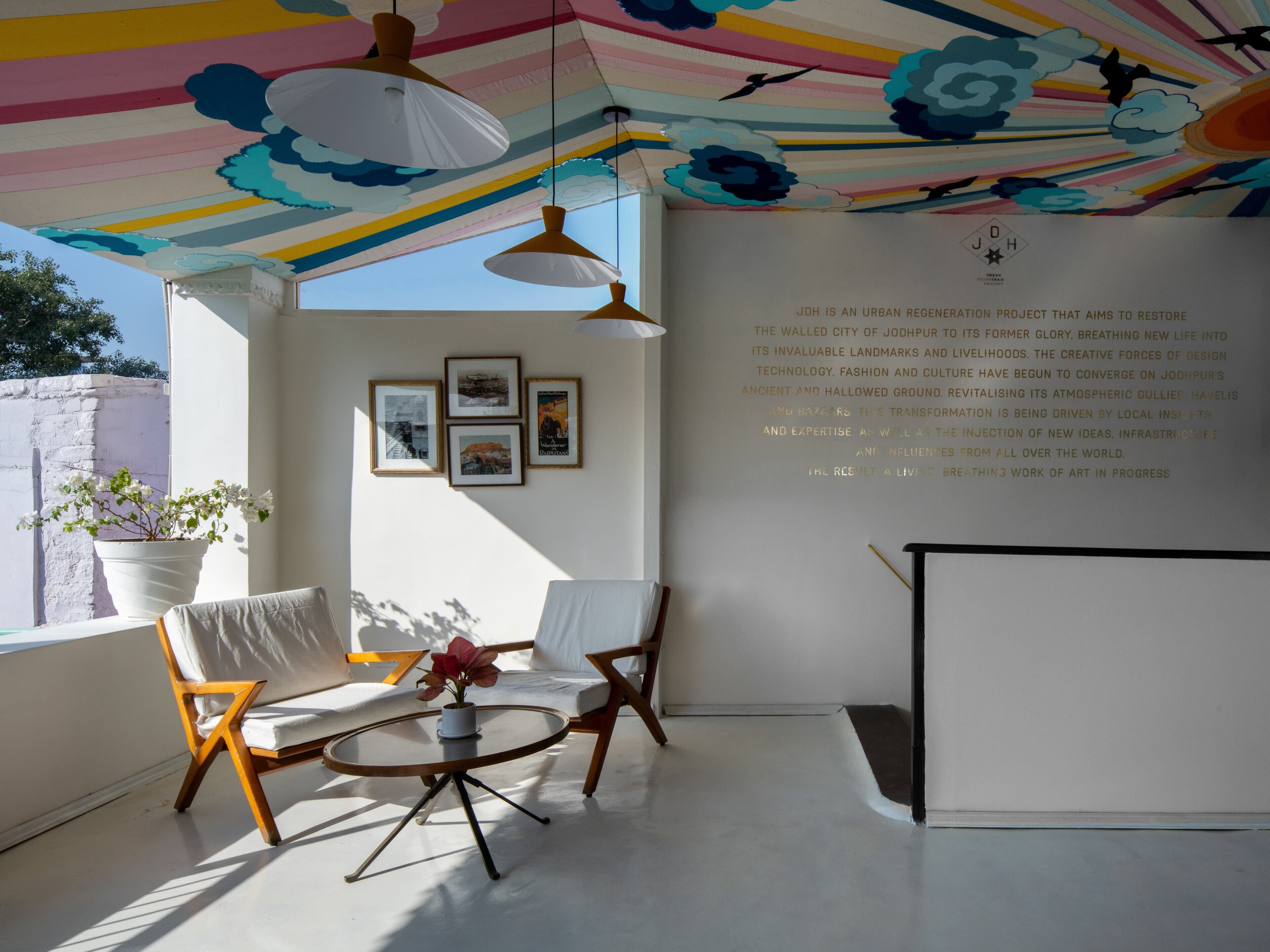 Een modern interieur met een witte muur, ingelijste foto's, een potplant en een plafond met een kleurrijk streepdessin.