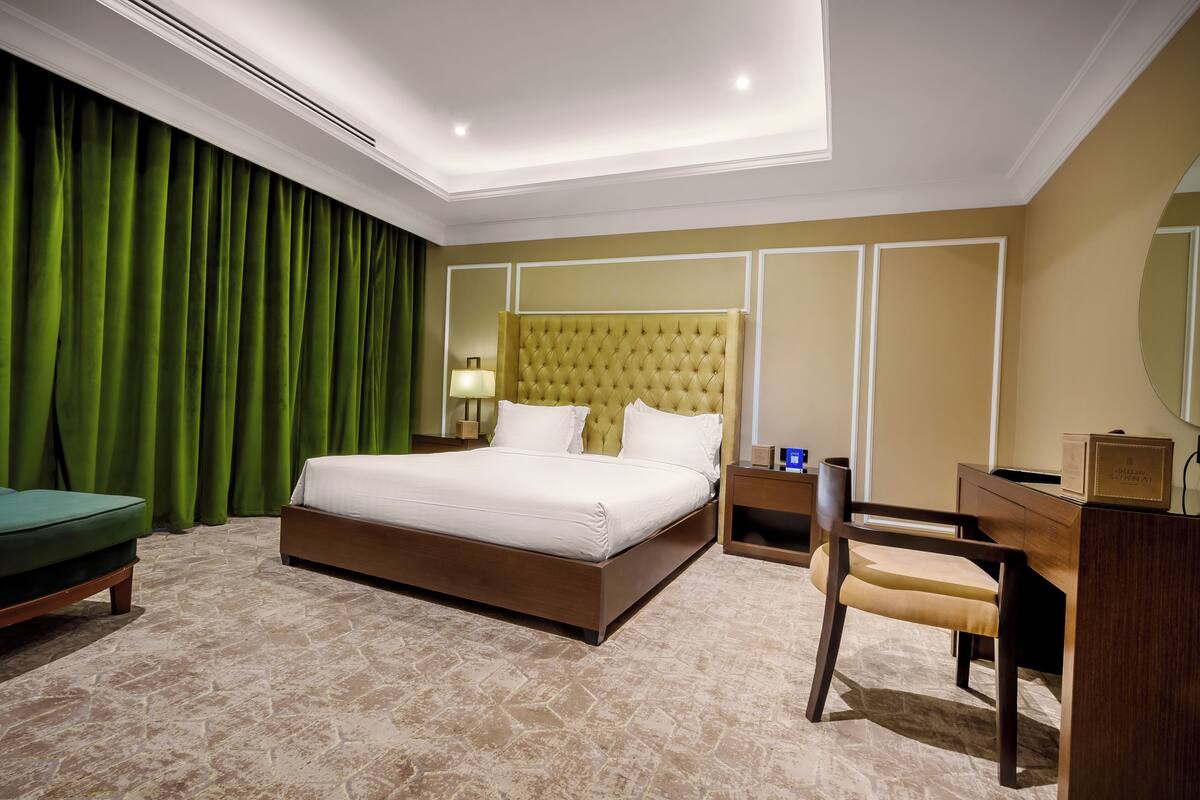 Una habitación de hotel con una cama grande, un escritorio, una silla, una mesita de noche y una cortina verde.