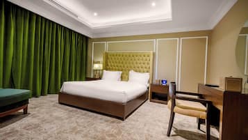 Een hotelkamer met een groot bed, een bureau, een stoel, een nachtkastje en een groen gordijn.