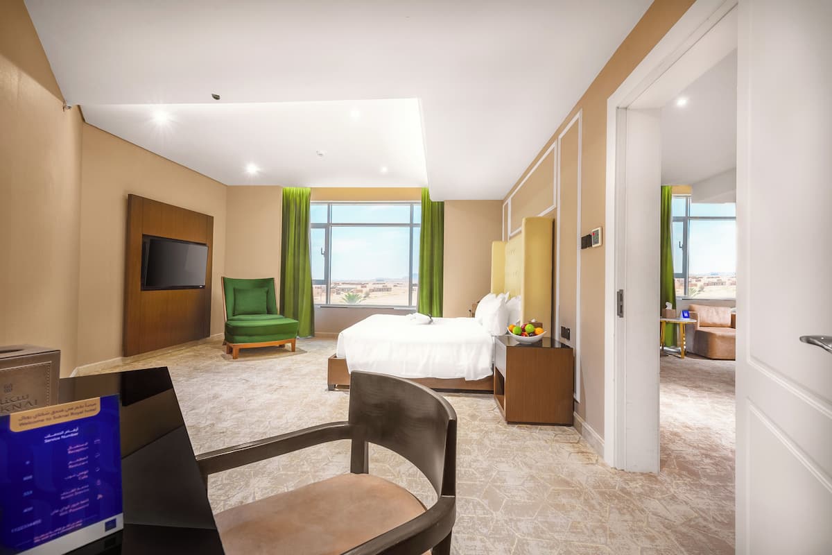 Habitación de hotel con cama, escritorio, silla, televisor y vista a la ciudad.
