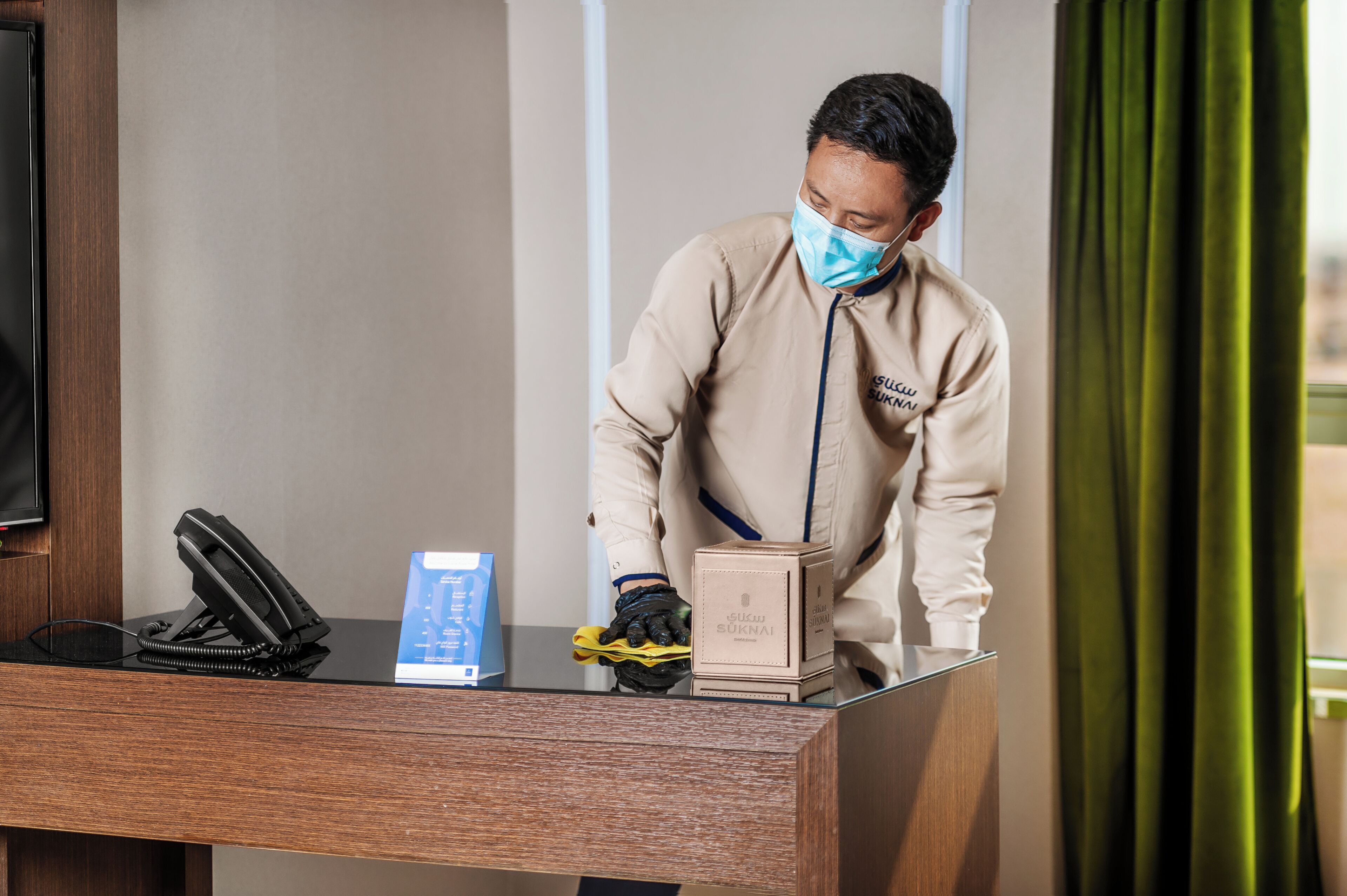 A hotel reception desk with a telephone, a blue informational brochure, and a box labeled "Sukhnai."