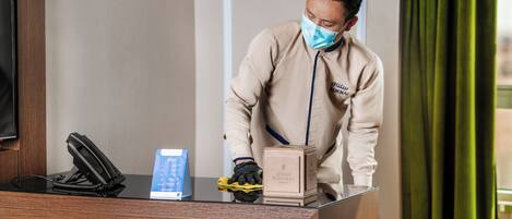 A hotel reception desk with a telephone, a blue informational brochure, and a box labeled "Sukhnai."