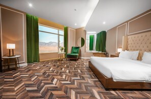 Habitació d'hotel amb un llit gran, una butaca verda, un mirall rodó i vista al desert per la finestra.