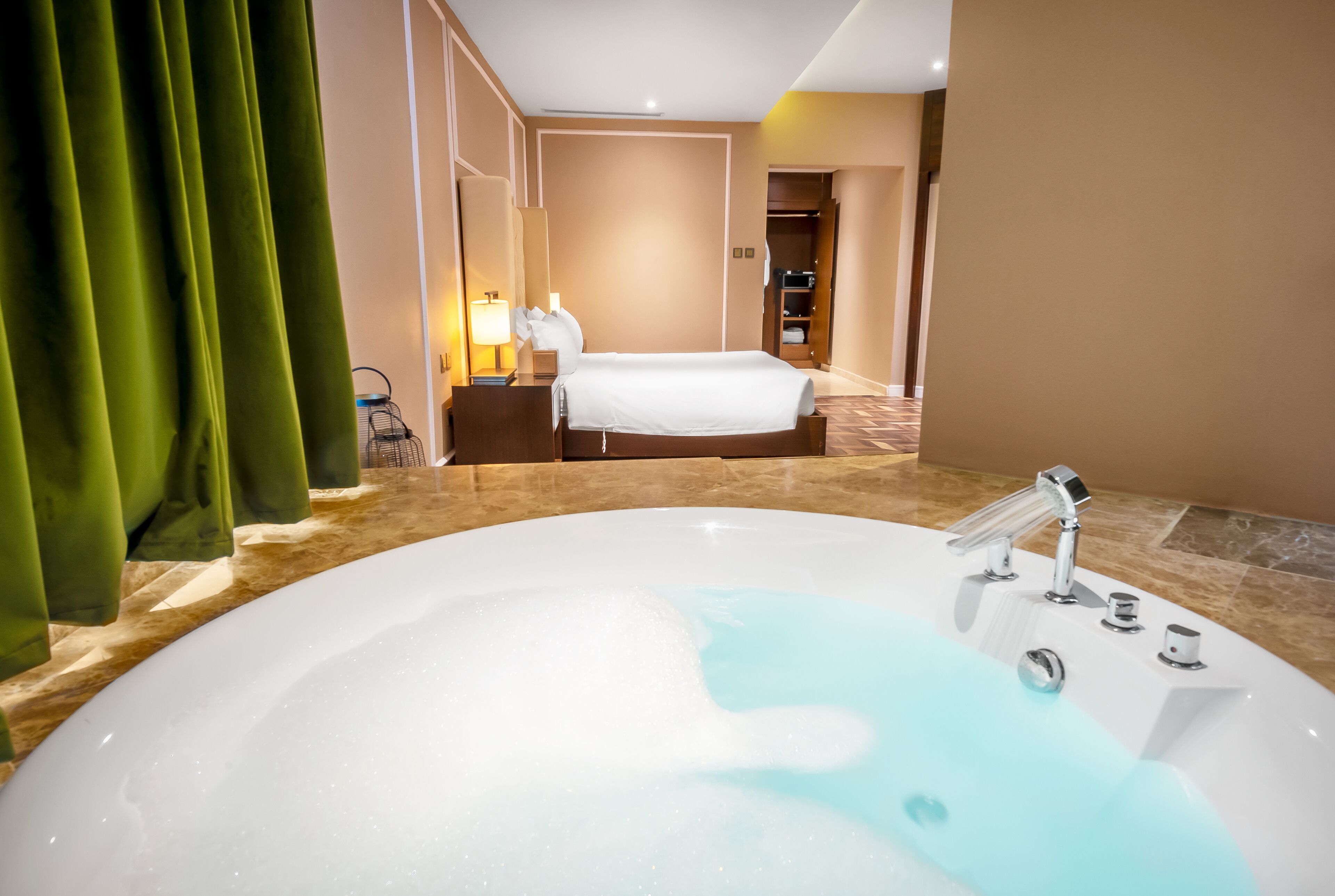 A hotel bathroom with a large bathtub, a separate shower area, a bed, and a vanity with a mirror.