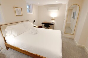 A neatly made bed with white linens, a desk with a lamp, and a large mirror on the wall. - Modern Apartment in the Heart of Logan Circle (Washington)