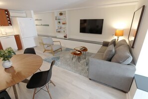 A modern living room with a grey sofa, a wooden dining table, and a TV mounted on the wall. - Modern Apartment in the Heart of Logan Circle (Washington)