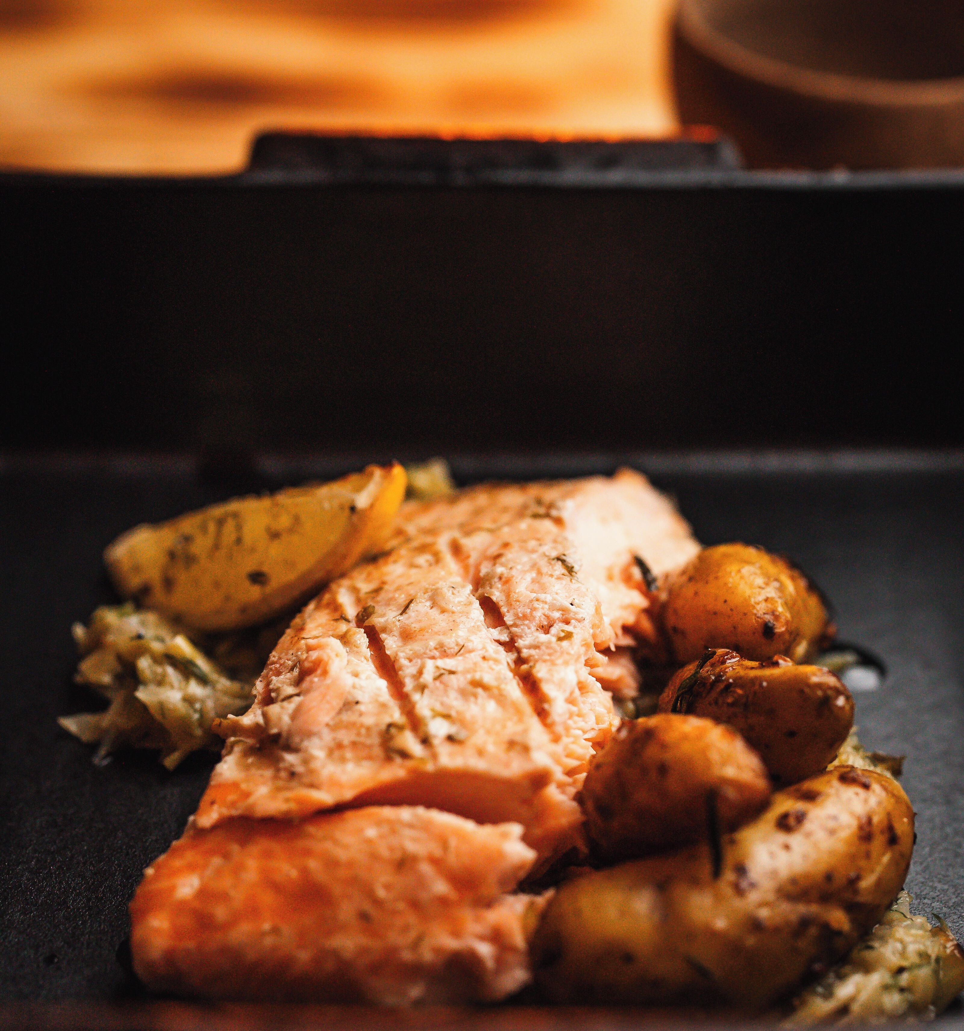 Un filet de saumon accompagné de pommes de terre rôties, le tout présenté sur une assiette foncée.