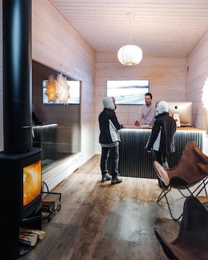 A room with a wood-burning stove, a large window, and a modern light fixture. - Nova Galaxy Village (Rovaniemi)