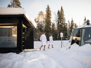 Una cabaña de madera cubierta de nieve con un puerta de cristal, rodeada de nieve y árboles.
