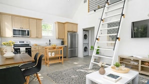A modern kitchen with wooden cabinets, a dining area with a table and chairs, a white coffee table, and a built-in washing machine. - Splash Pad (Atlanta)