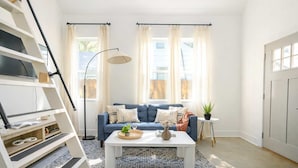 A modern living room with a blue sofa, white coffee table, and a patterned rug. There is a staircase on the left, a floor lamp, and a potted plant on a small table. - Splash Pad (Atlanta)