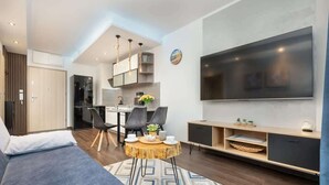 A modern living room with a sofa, dining table, chairs, and a TV. - Stylish Apartment with Balcony | Parking in Garage (Świnoujście)