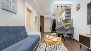 A modern living room with a sofa, a round wooden coffee table, and a dining area with chairs and a kitchen in the background. - Stylish Apartment with Balcony | Parking in Garage (Świnoujście)
