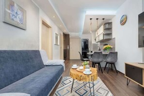 Una sala moderna con un sofá, una mesa de centro redonda de madera y una zona de comedor con sillas, con una cocina al fondo.
