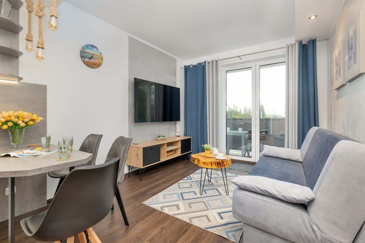 Ein modernes Wohnzimmer mit einer Couch, einem Esstisch, Stühlen, einem Fernseher und einem großen Fenster mit Vorhängen.
