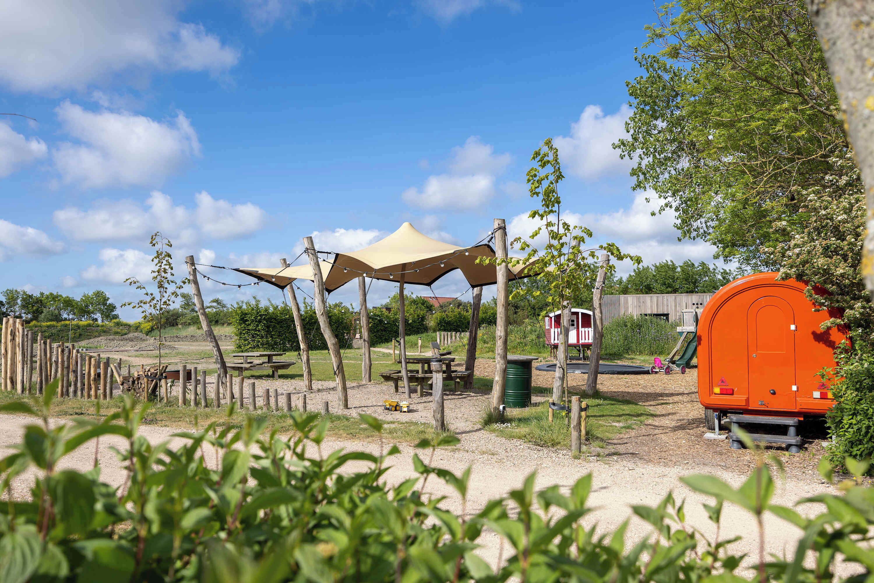 Een camping met tenten, een picknicktafel, een speelplaats en een draagbaar toilet.