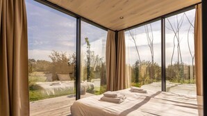 A bedroom with a large window, a bed, and a view of the outdoors.