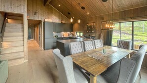A modern kitchen with a central island, a dining area with a wooden table and cushioned chairs, and a view of the outdoors through large windows. - Nice home in Trysil with house a mountain view (Trysil)
