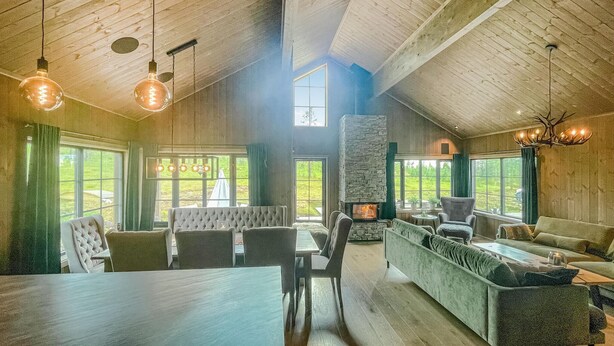 A spacious living room with a high ceiling, a stone fireplace, and large windows offering a view of the outdoors. - Nice home in Trysil with house a mountain view (Trysil)