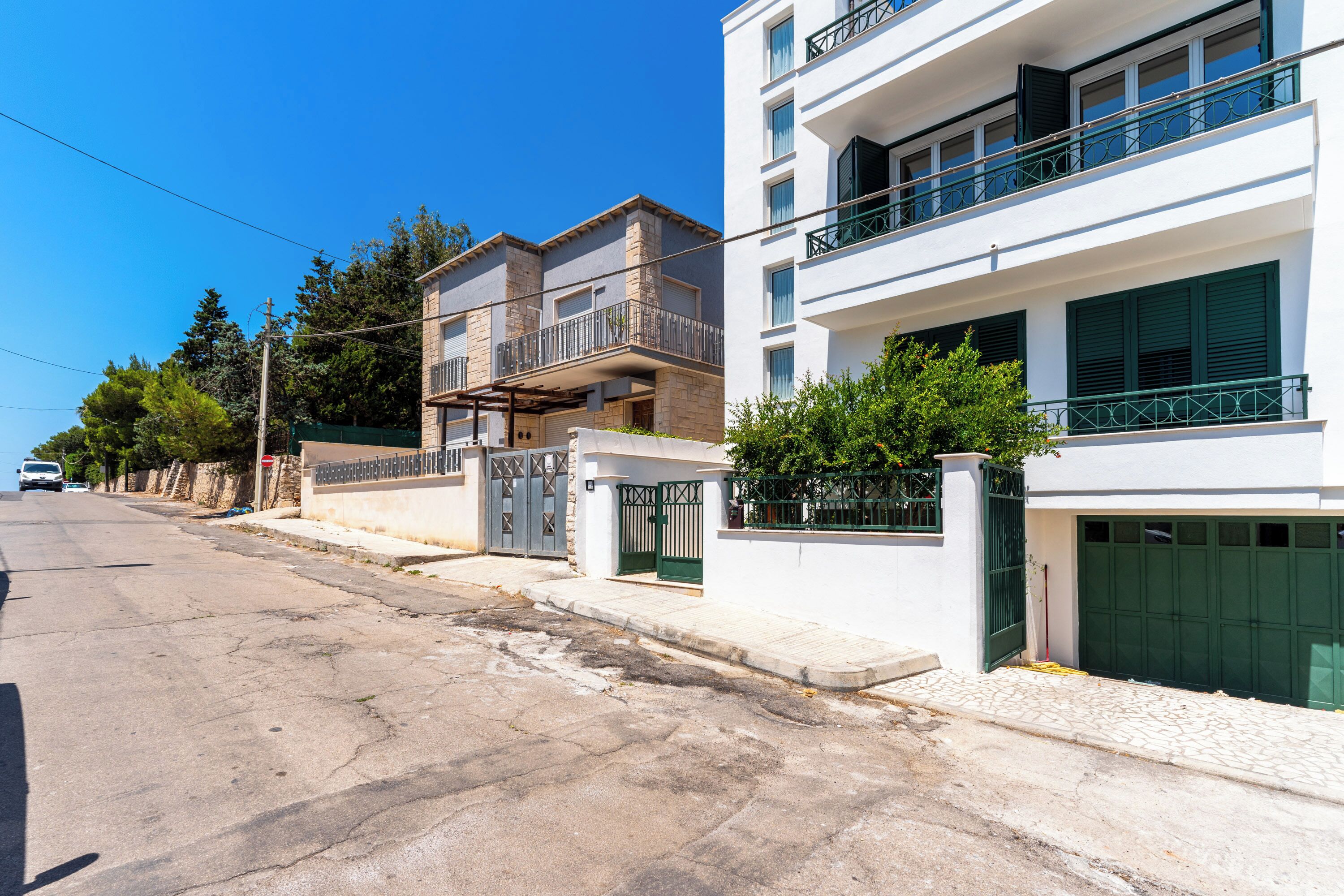 A residential building with multiple balconies, a gated entrance, and a paved driveway.
