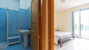 A bathroom with a shower, sink, and toilet. There is a bed with a view to the outside.