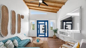 Un salon moderne avec un plafond en bois, une porte bleue et un téléviseur à écran plat fixé au mur.