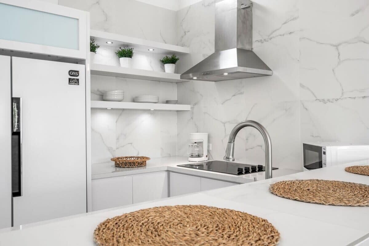 Een moderne keuken met witte kastjes, een roestvrijstalen afzuigkap en een marmeren spatwand.