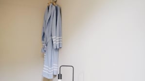 Quarto com cama, almofadas, um roupão pendurado na parede e uma luminária de cabeceira.