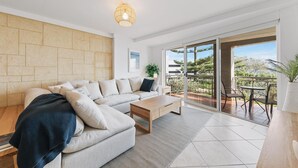 A modern living room with a sofa, coffee table, and a balcony with outdoor seating. - Apartment M204 - coastal and comfortable! (Scarborough)
