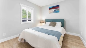 Un dormitorio con cama, ventana con persianas, un cuadro en la pared y una lámpara.
