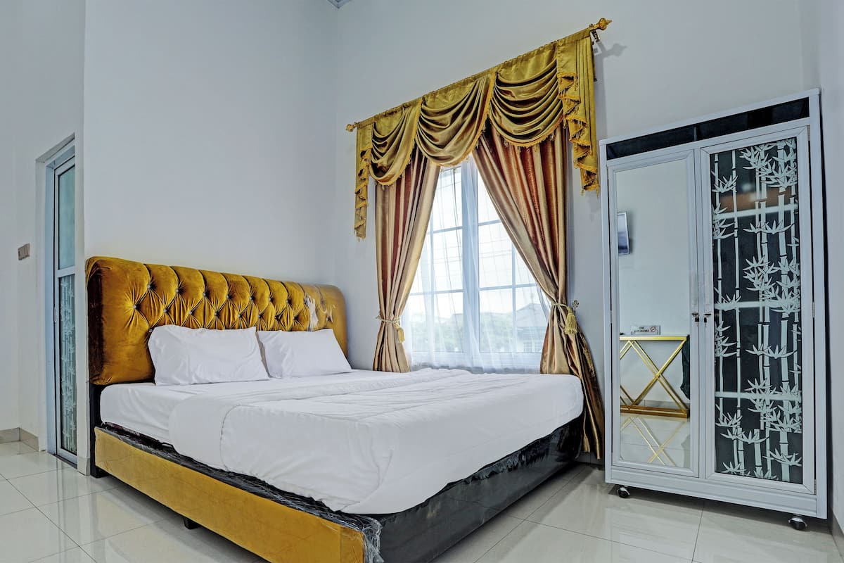 A neatly made bed with a golden headboard, a wardrobe with a decorative glass panel, and a window with curtains.
