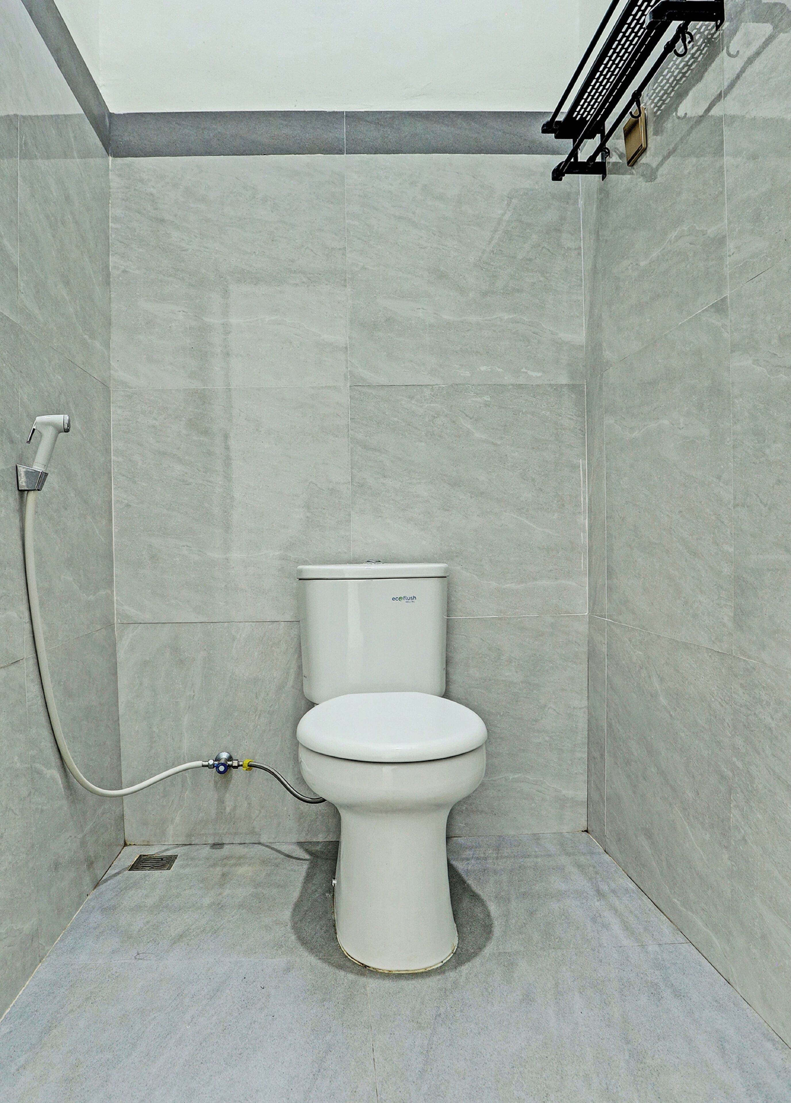 Ein Badezimmer mit Toilette, grauen Fliesenwänden und einer Duschkabine.