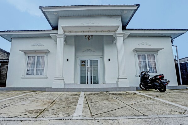 A white building with a central entrance, columns, and a motorcycle parked in front.