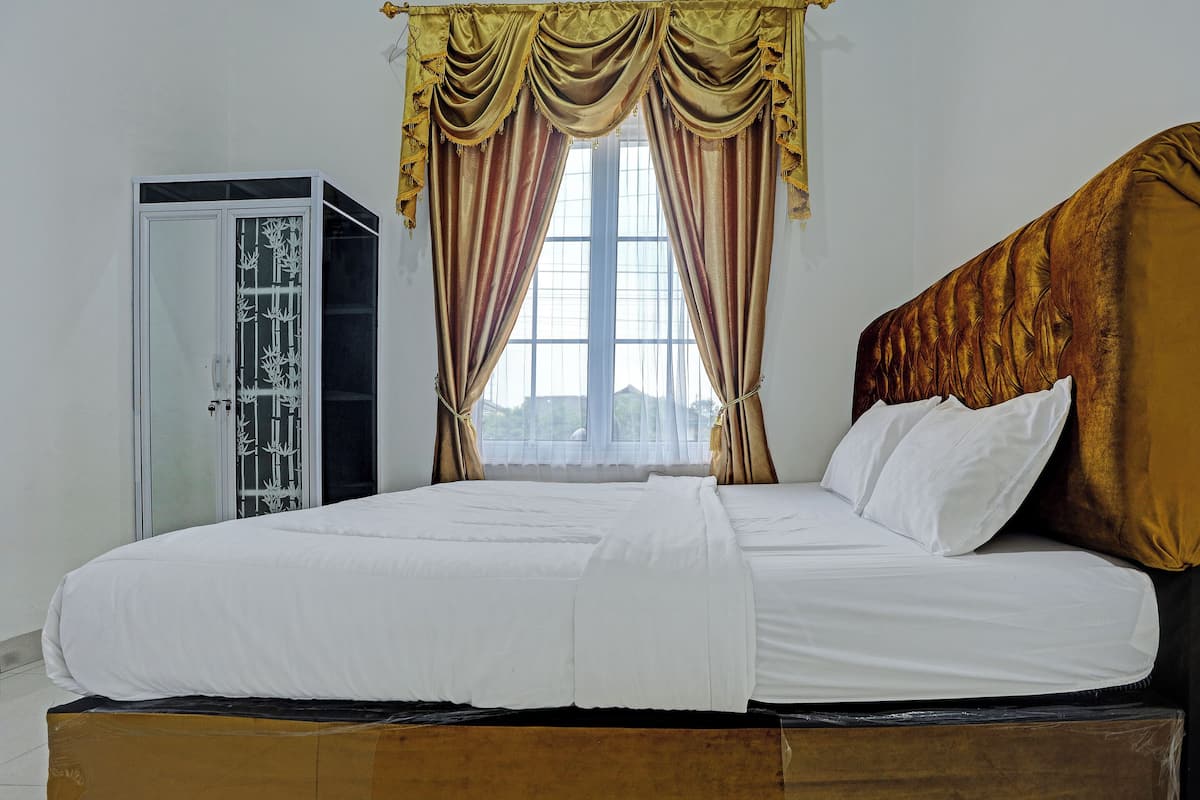 A neatly made bed with white linens, a wooden headboard, and a window with curtains.