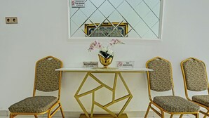 A reception desk with a gold geometric base, two patterned chairs, a vase with flowers, and a sign indicating no smoking.