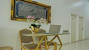 A reception area with a laptop on a desk, a framed Quran, and patterned chairs.