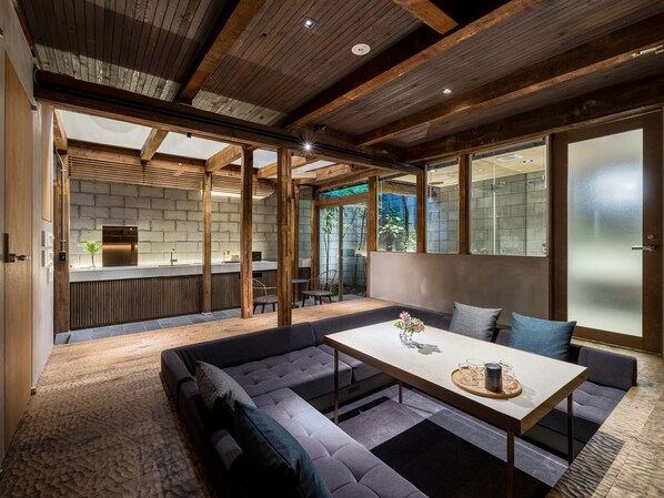 Een modern interieur met een houten plafond, een zithoek met een tafel, en een keuken die door een open deur zichtbaar is.