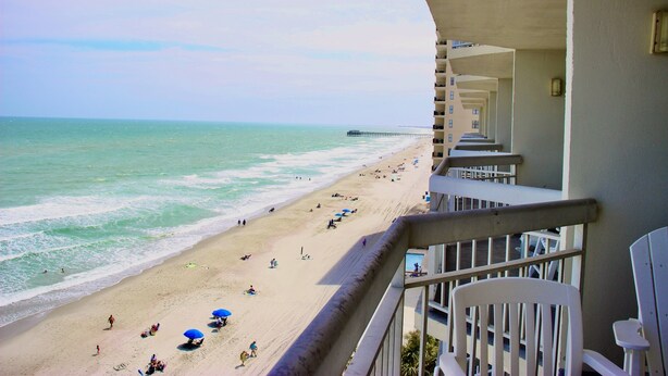 A beach view from a balcony with a pier in the distance. - Garden City Beach Oceanfront Condo 807 | Rising Tides Properties Rental (Murrells)