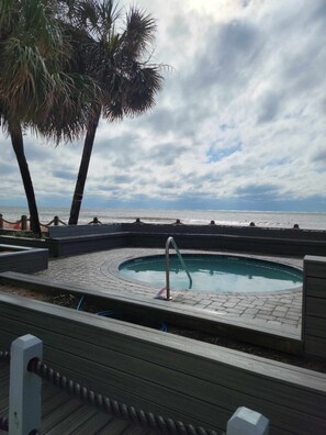 Relax by the ocean-view pool surrounded by palm trees and a wooden deck with steps leading down to the water.
