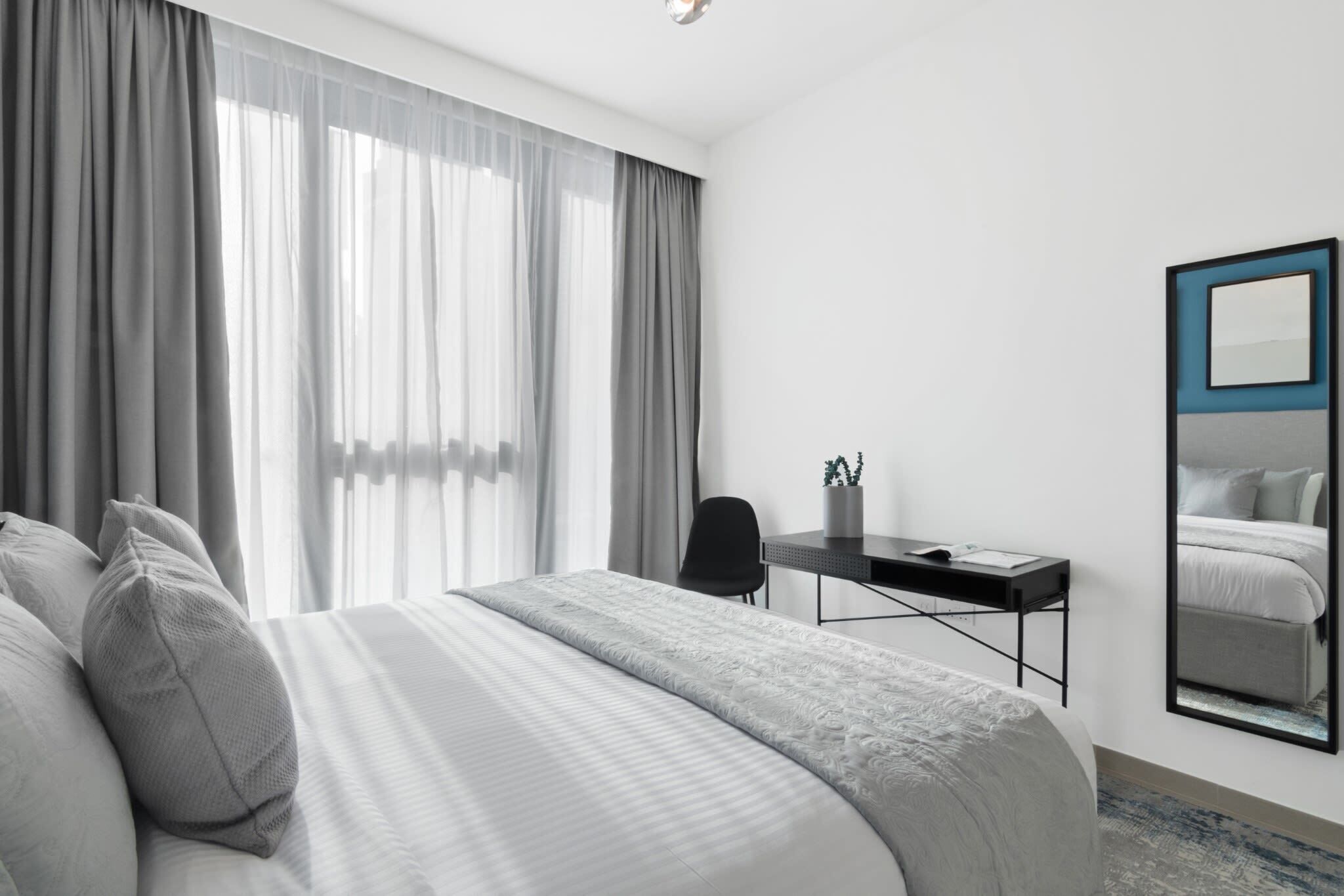 A modern hotel room with a large bed, a desk, and a mirror.
