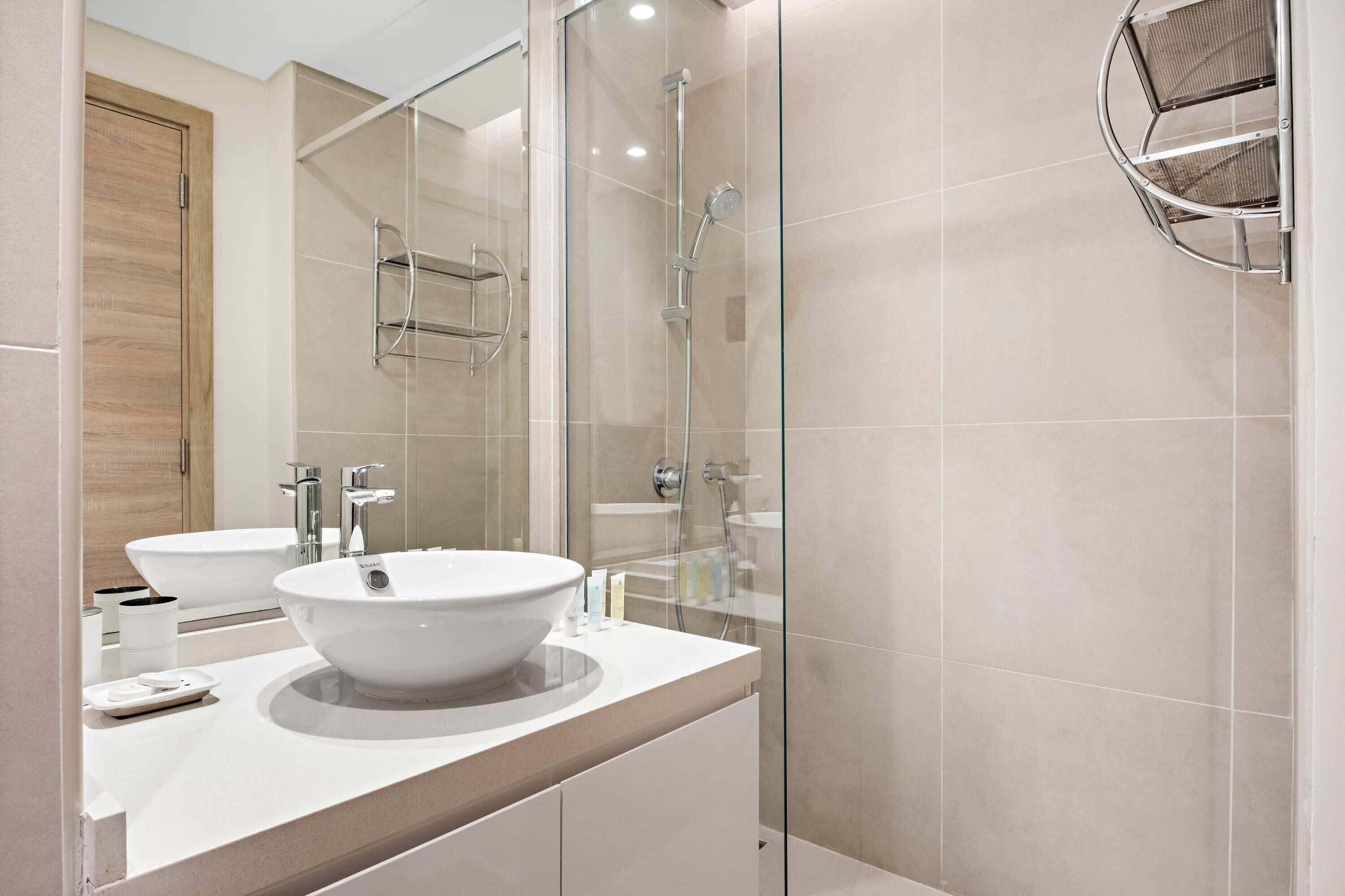 A modern bathroom with a large white sink, two mirrors, a glass shower enclosure, and a wooden door.