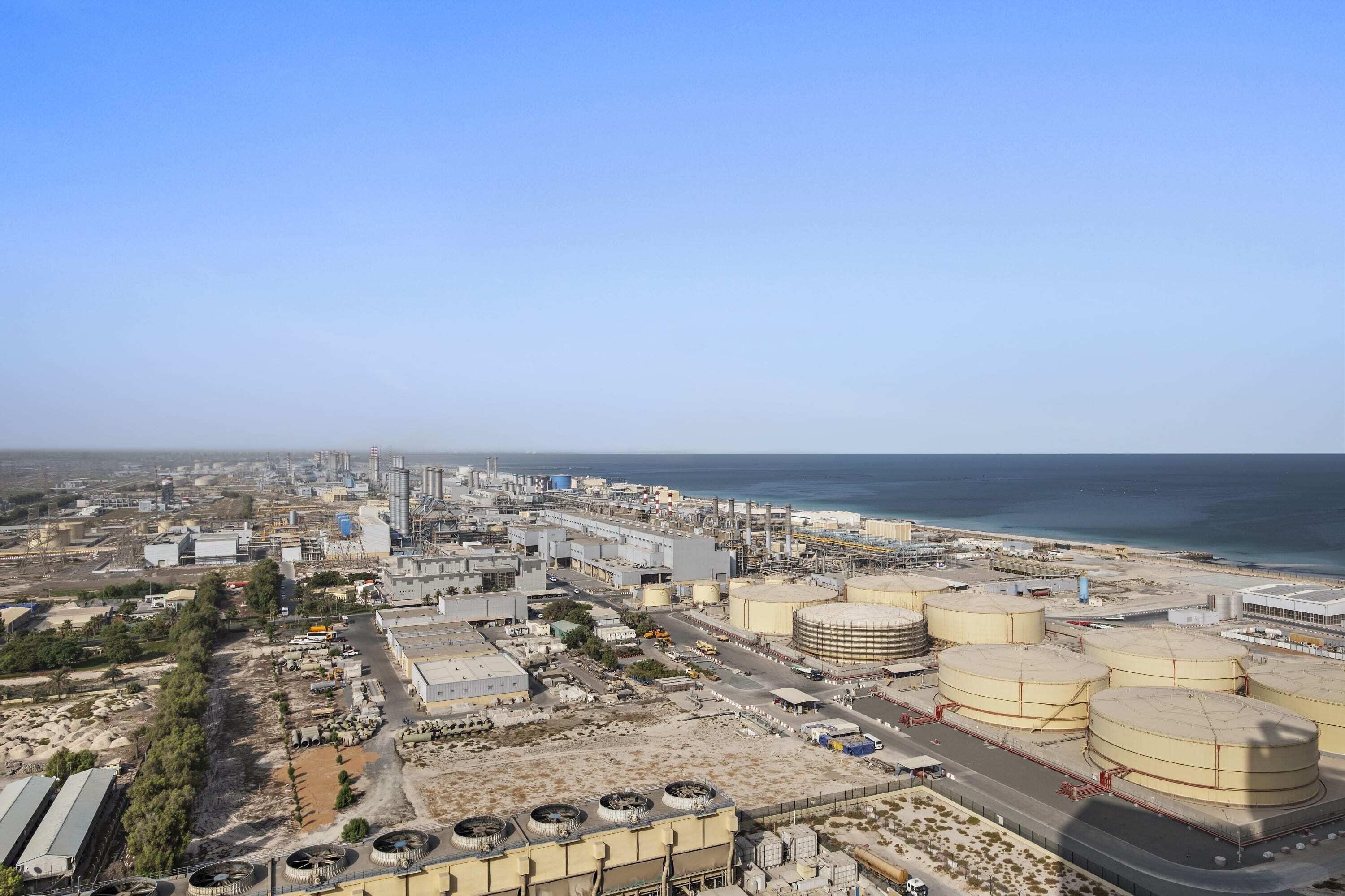 An industrial area with large storage tanks, a road, and a body of water in the background.