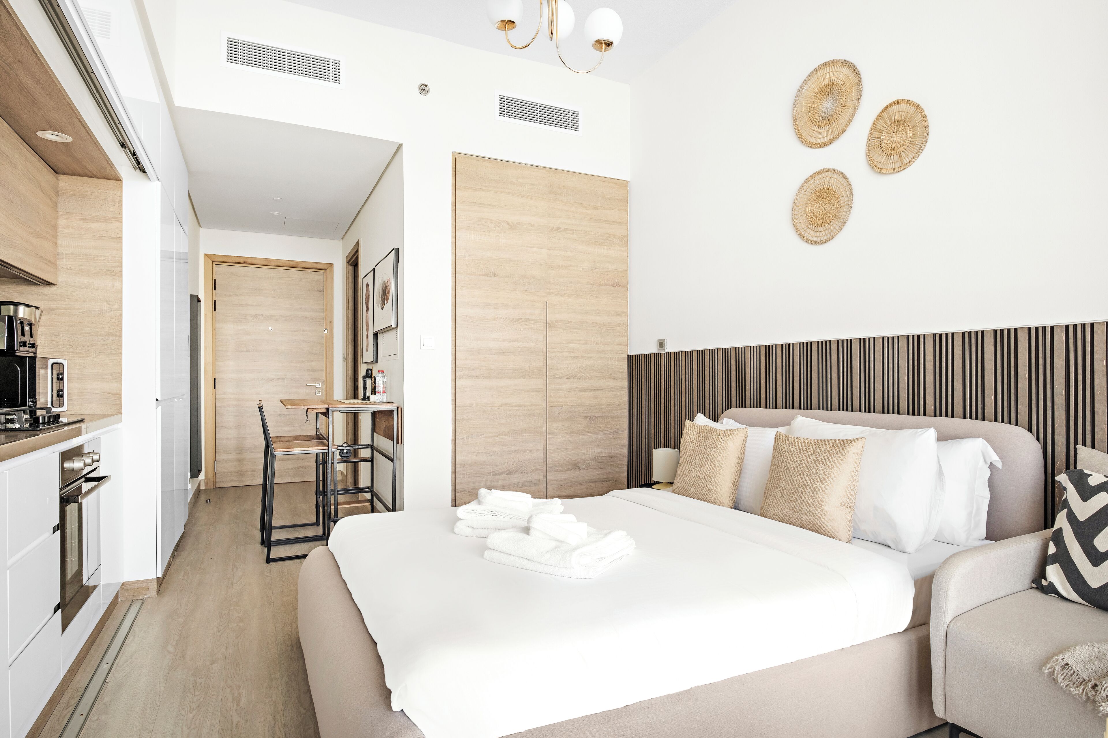 A modern hotel room with a bed, a sofa, a dining area, and a kitchenette.