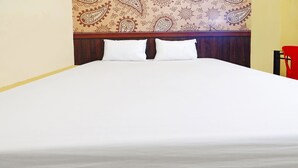 A bed with white linens and two pillows, a wooden headboard with a paisley pattern, and a red chair to the right. - OYO 92710 Losmen Tjabe Merah (Mataram)