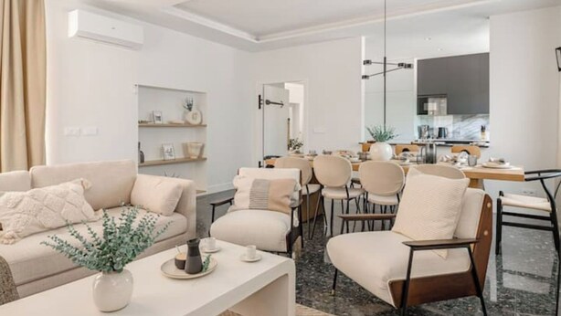 Ein modernes Wohnzimmer mit einer Couch, Sesseln, einem Couchtisch und einem Essbereich mit Stühlen und einem Tisch.