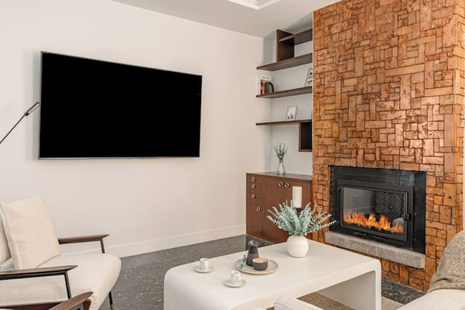 Un salon moderne doté d’un téléviseur à écran plat fixé au mur, d’une cheminée à la façade en briques et d’une table basse minimaliste agrémentée d’objets décoratifs.