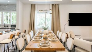 Ein moderner Essbereich mit einem langen Holztisch, gedeckt für eine Mahlzeit, umgeben von weißen Stühlen.