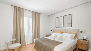Ein modernes Schlafzimmer mit einem großen Bett, einem Nachttisch, einem Sessel und einem Fenster mit Vorhängen.